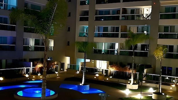 A multi-story hotel with a courtyard featuring a water feature and seating areas. - Brisas do Lago - apartamento 7 (Brasília)