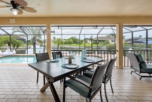 A covered patio with a dining table and chairs, a pool, and a view of the surrounding landscape. - Canalfront/Outdoor Kitchen/Pool/Spa/Boat Dock (Cape Coral)