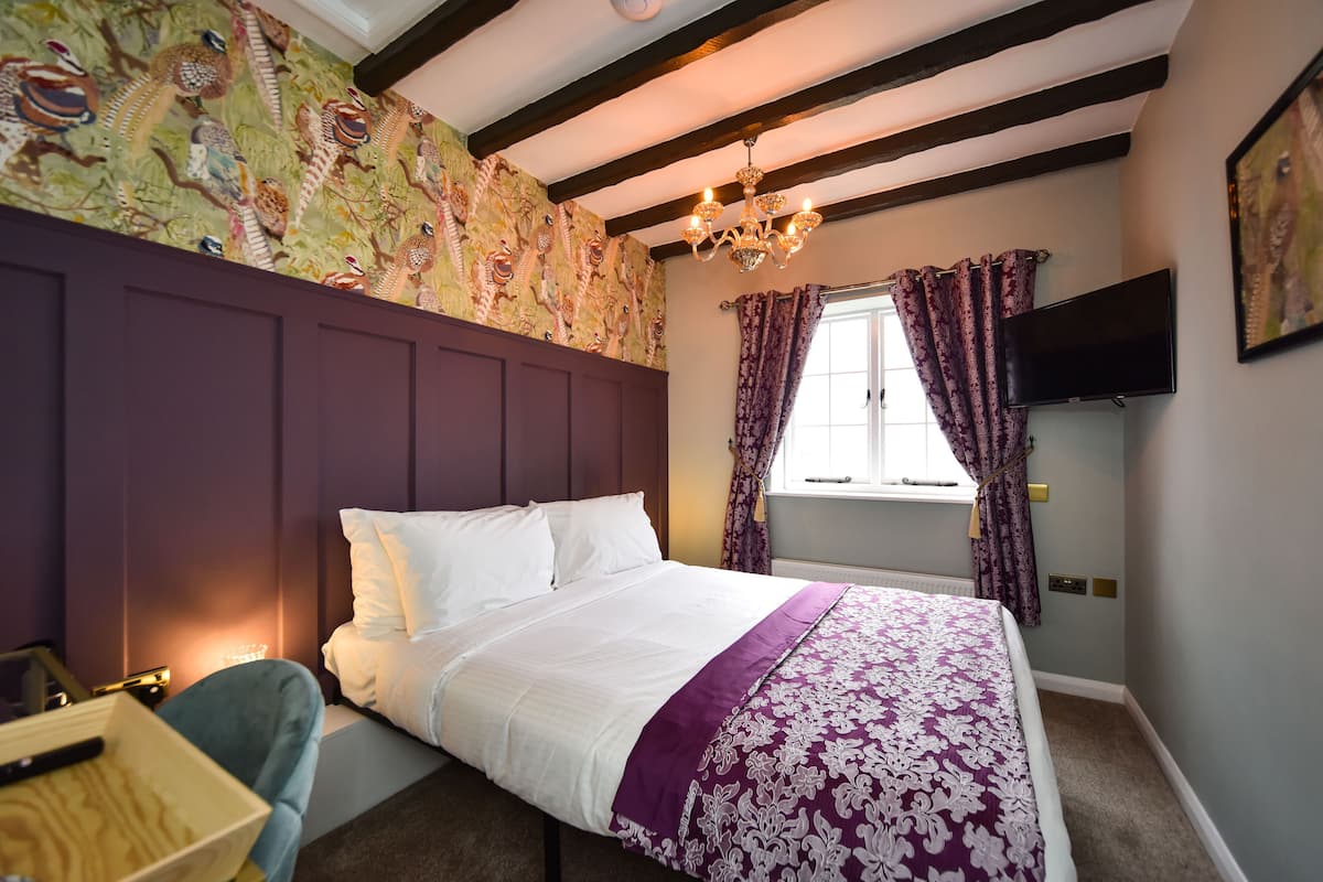 Een slaapkamer met een groot bed, een houten nachtkastje, een bureau, een stoel, een televisie en een raam met gordijnen.