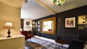 Une pièce avec un tapis à carreaux, un fauteuil rouge, un canapé noir, une table et un lustre en vitrail.