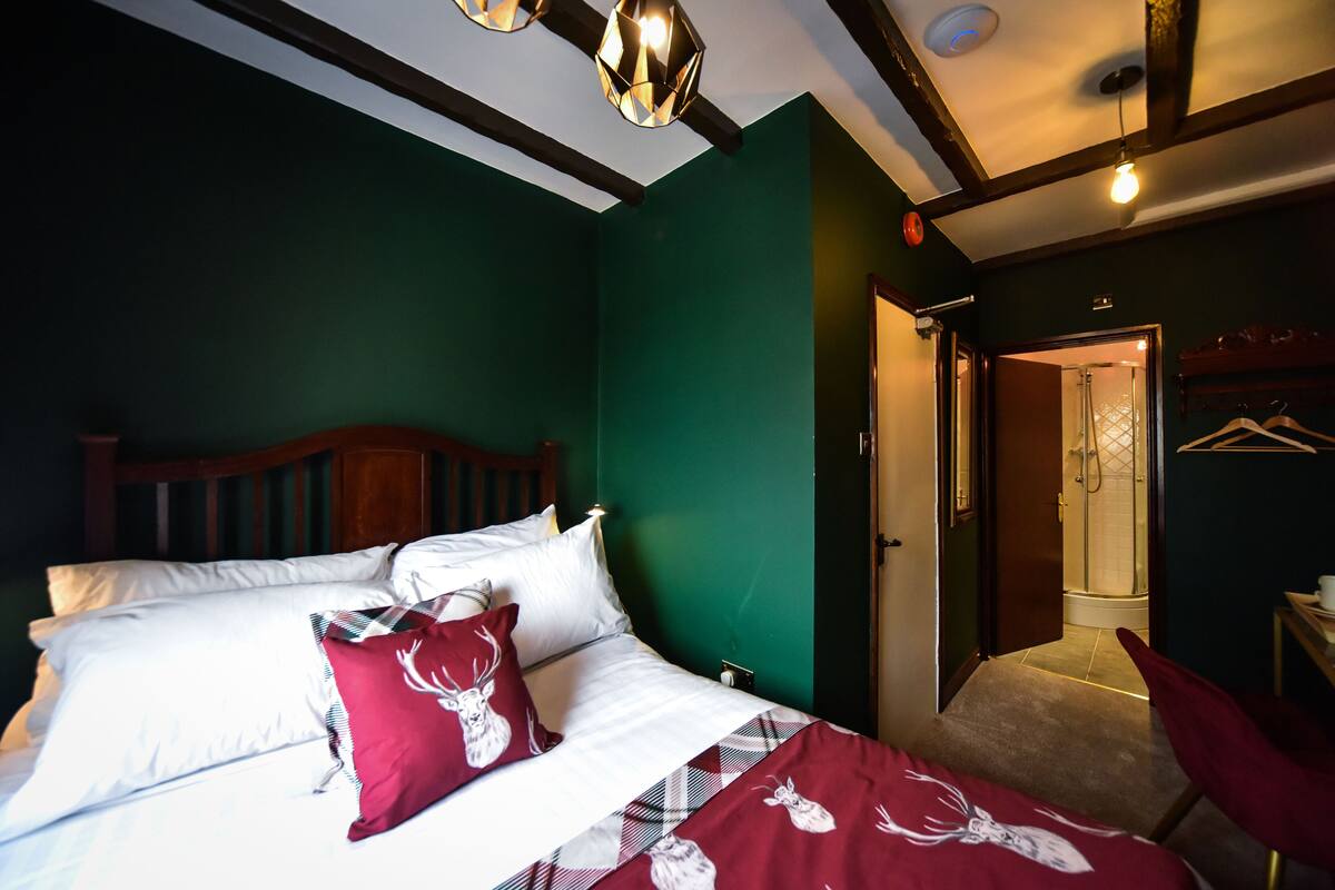 Een slaapkamer met een bed, kussens en een dekbed. Er is een deur naar een badkamer.