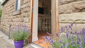 Un bâtiment en pierre avec une porte en bois et un pot de fleurs violet placé à l’extérieur.