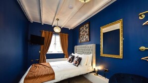 Une chambre à coucher avec un grand lit, une télévision, une fenêtre avec des rideaux et un miroir fixé au mur.