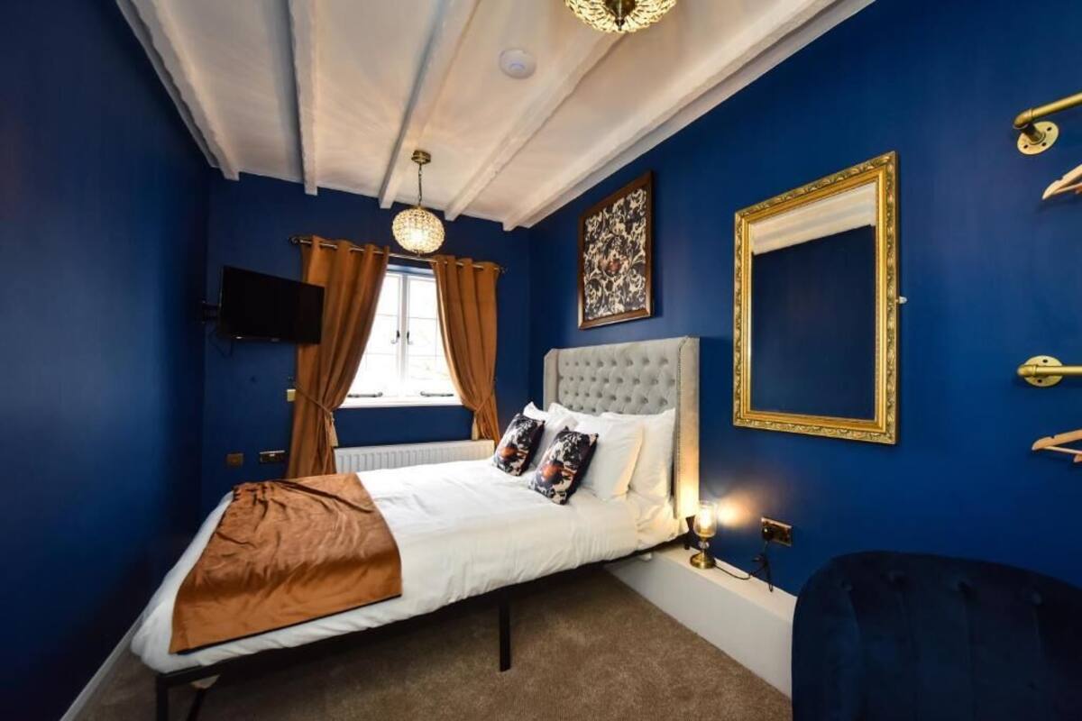 Een slaapkamer met een groot bed, een televisie, een raam met gordijnen en een spiegel aan de muur.