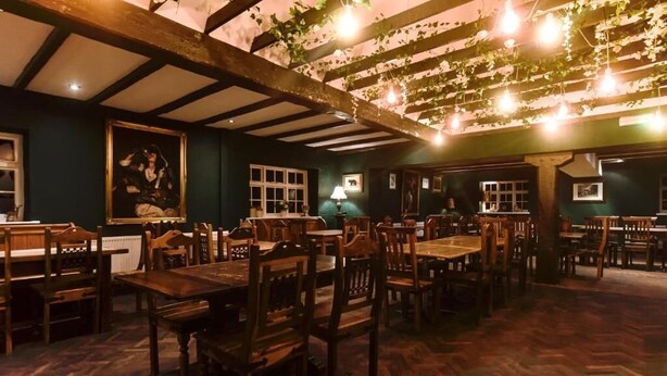 Un restaurant avec des tables et des chaises en bois, un plafond haut avec des poutres apparentes et des luminaires suspendus.
