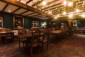 A restaurant with wooden tables and chairs, a high ceiling with exposed beams, and hanging lights.