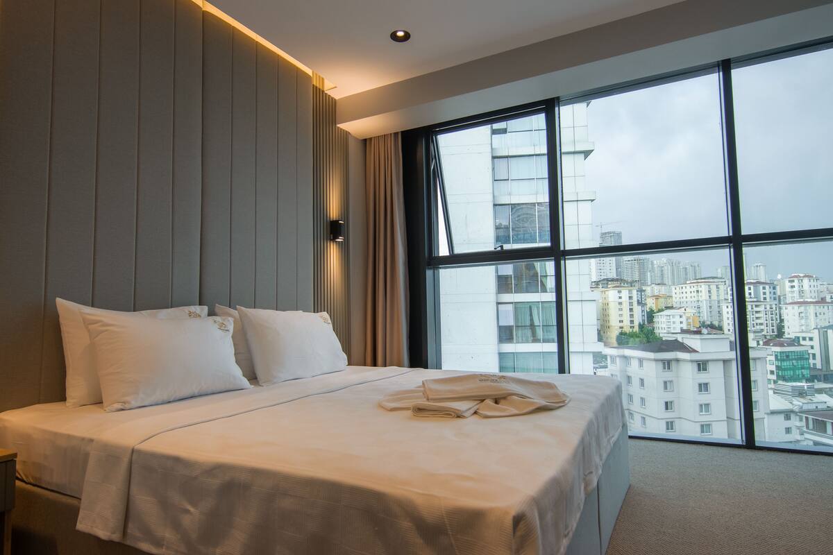 A hotel room with a large window, a bed with white linens, and a city view.