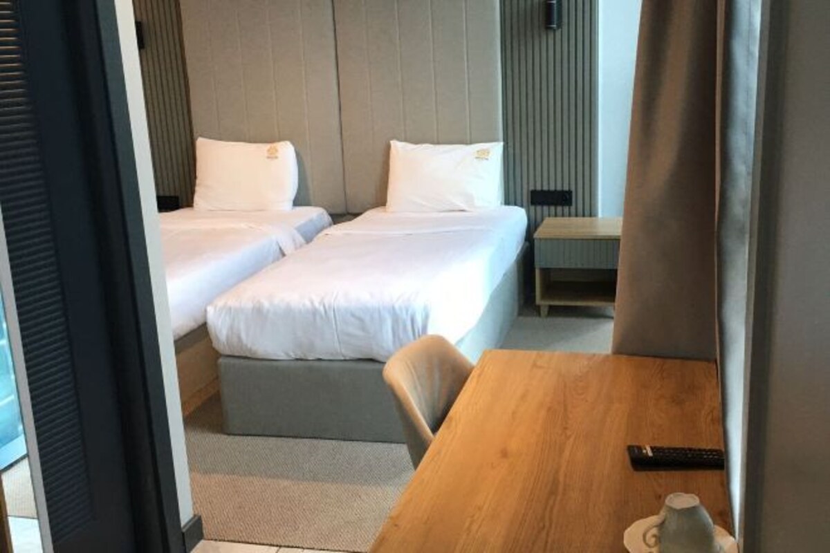 A hotel room with two beds, a wooden table, a chair, and a remote control on the table.