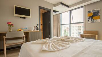 A hotel room with a bed, a desk, a chair, a TV, and a window with a city view.