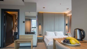 Una habitación de hotel moderna con cama, mesita de noche y bandeja de desayuno con frutas.