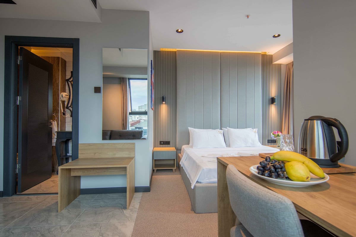 A modern hotel room with a bed, bedside table, and a breakfast tray with fruits.
