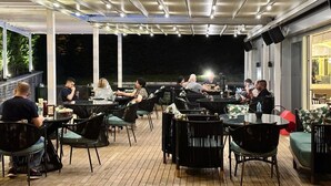 Un espacio de comedor al aire libre con mesas y sillas, cubierto por un techo con luces.