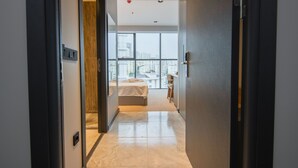 Una habitación de hotel moderna con un ventanal grande, una cama y una pequeña zona de escritorio.