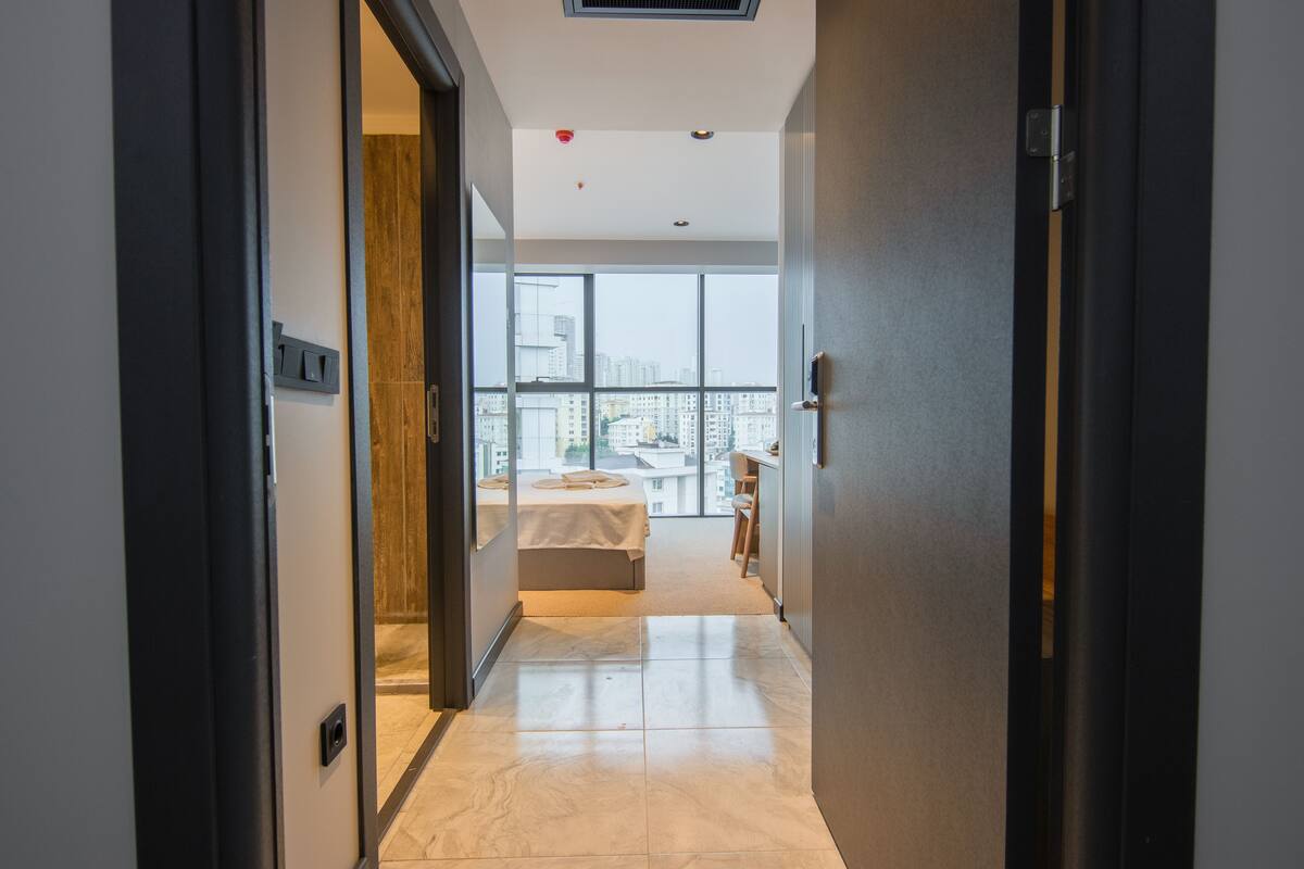 A modern hotel room with a large window, a bed, and a small desk area.