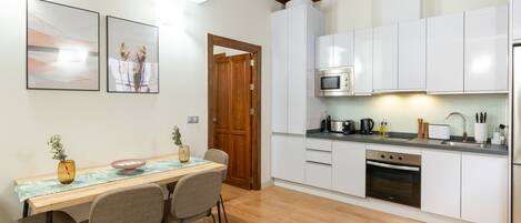 A modern kitchen with white cabinets, a microwave, and a stove. There is a dining table with chairs and a vase of flowers.
