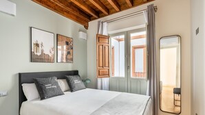 Un dormitorio con una cama, un espejo, una ventana con cortinas y una obra de arte en la pared.