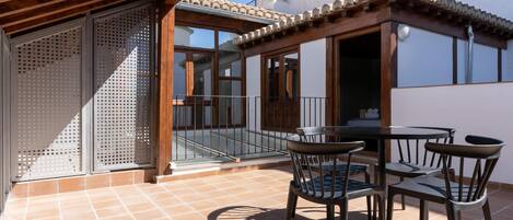 Un patio exterior con una pérgola de madera, un ventanal de vidrio que da a un balcón y una mesa con sillas.