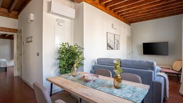 Una sala de estar moderna con techo de madera, un sofá gris, un televisor montado en la pared y un comedor con mesa y sillas de madera.