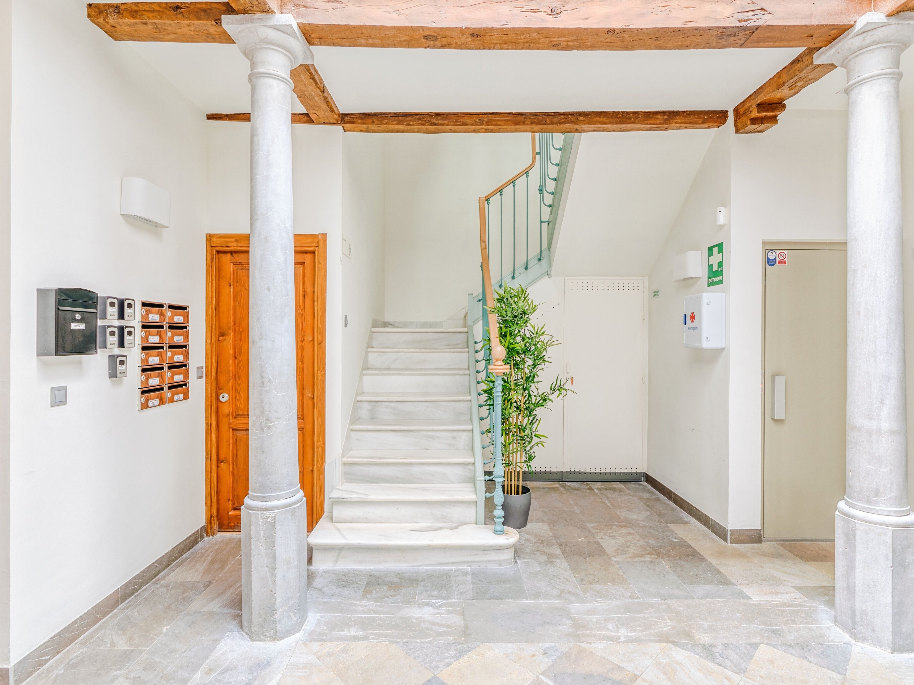 A spacious hallway with a marble floor, a wooden door, and a staircase with a green railing.
