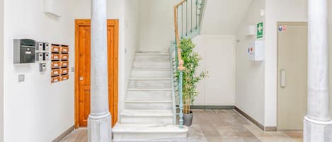 A spacious hallway with a marble floor, a wooden door, and a staircase with a green railing.