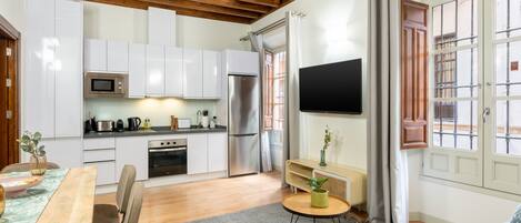 Una cocina compacta con electrodomésticos modernos, un comedor con mesa y sillas, y una sala de estar con sofá y mesa de centro.