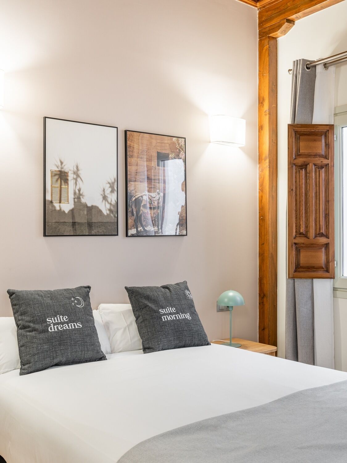 A bedroom with a bed, two pillows, a nightstand, a lamp, and two framed pictures on the wall.