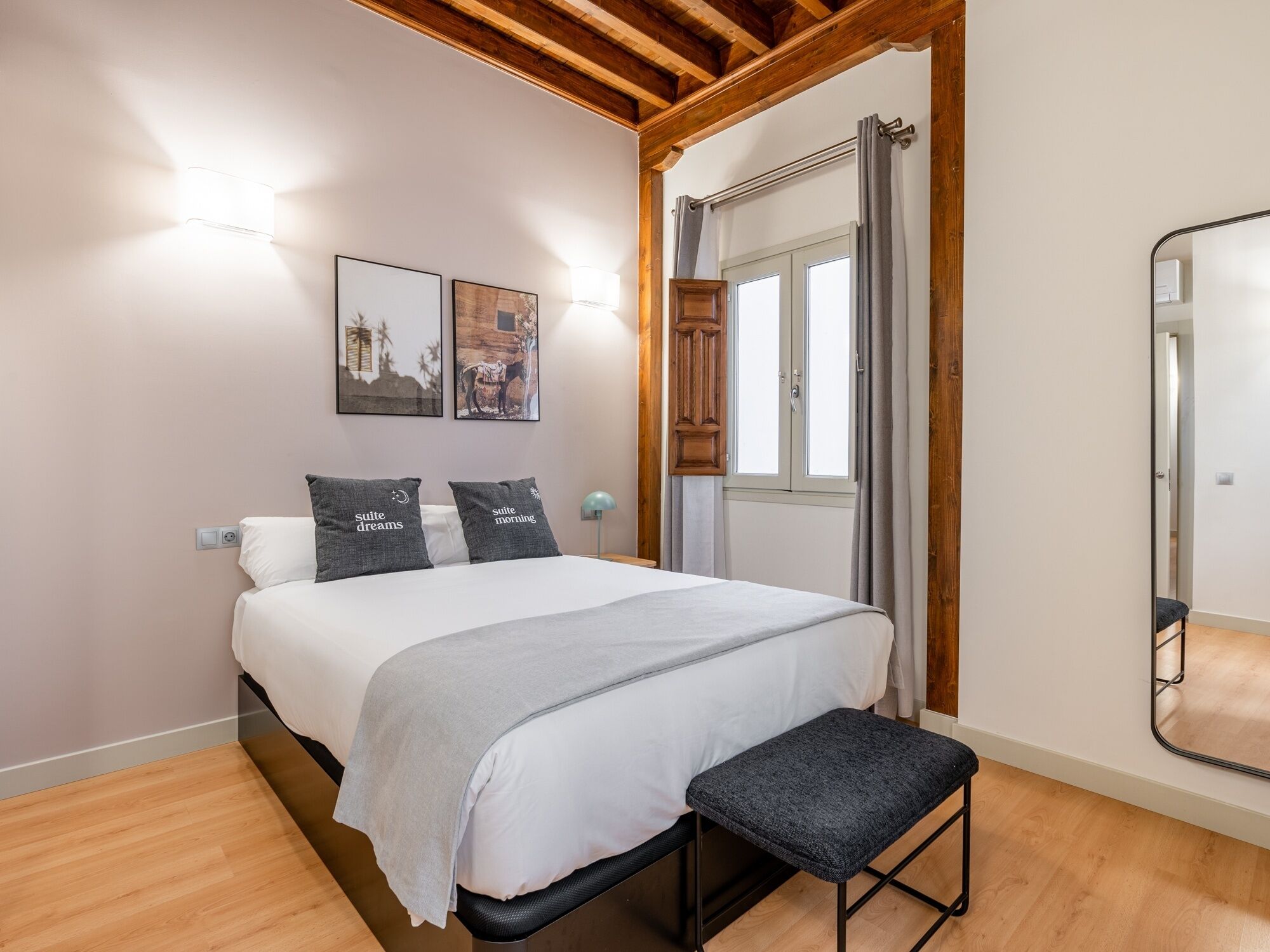 A bedroom with a bed, a bench, a mirror, and two wall-mounted lights.