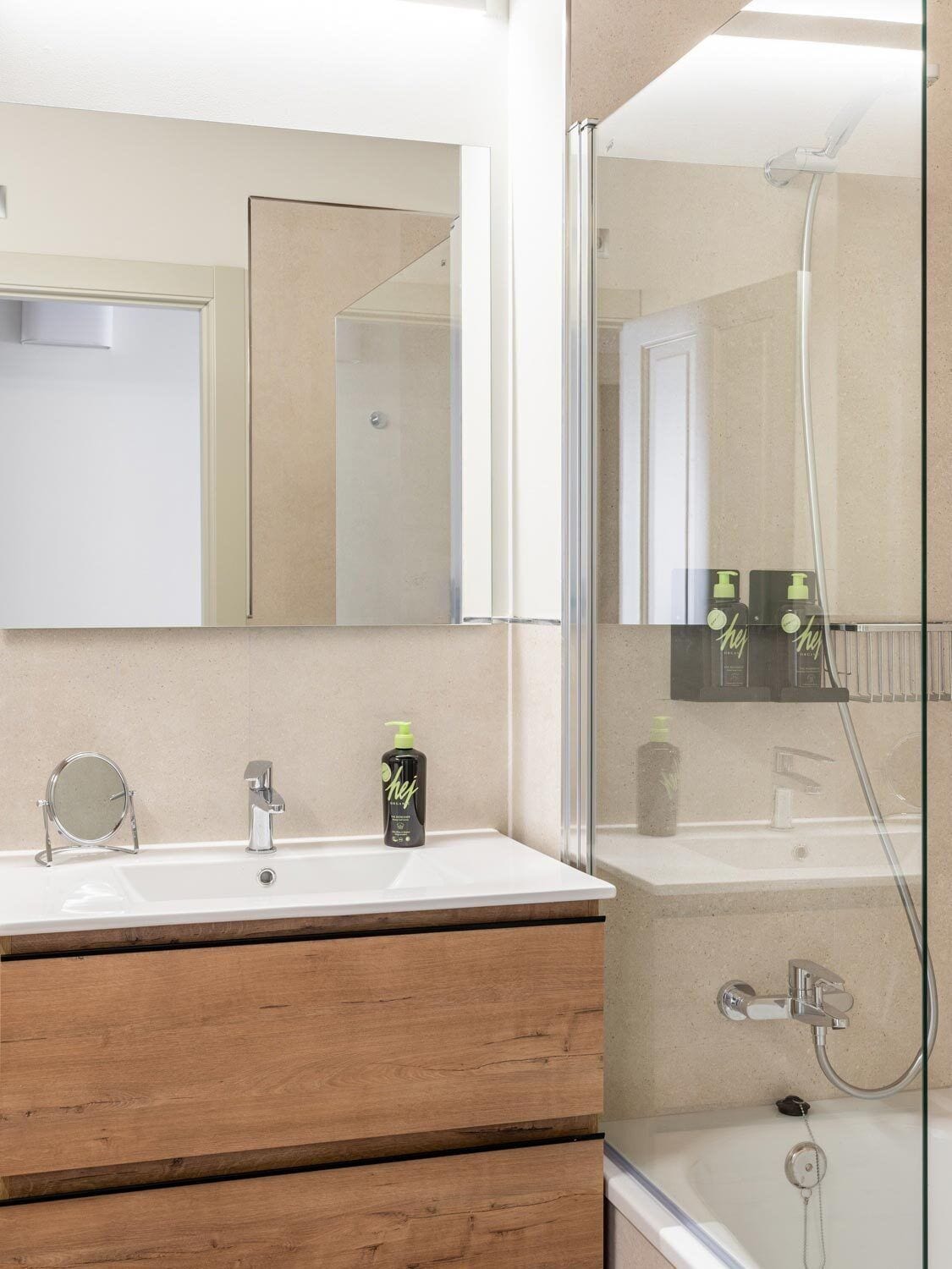 A modern bathroom with a large mirror, a sink, a wooden vanity, and a glass-enclosed shower area.