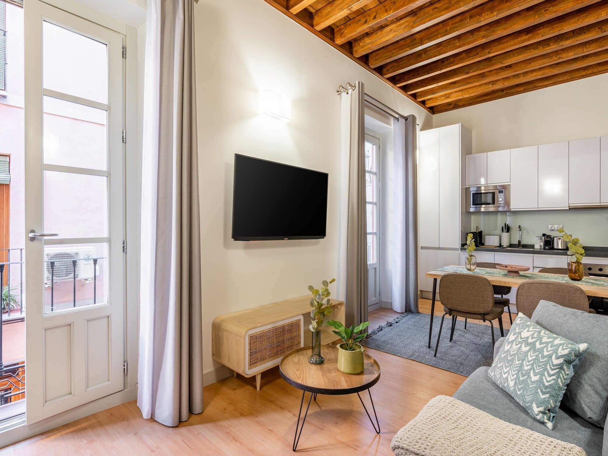 Una sala moderna con una televisión de pantalla plana, un sofá, una mesa de comedor y una cocina al fondo.