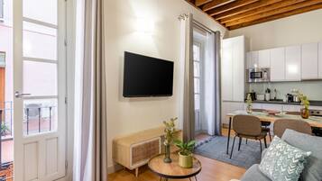 Una sala moderna con una televisión de pantalla plana, un sofá, una mesa de comedor y una cocina al fondo.