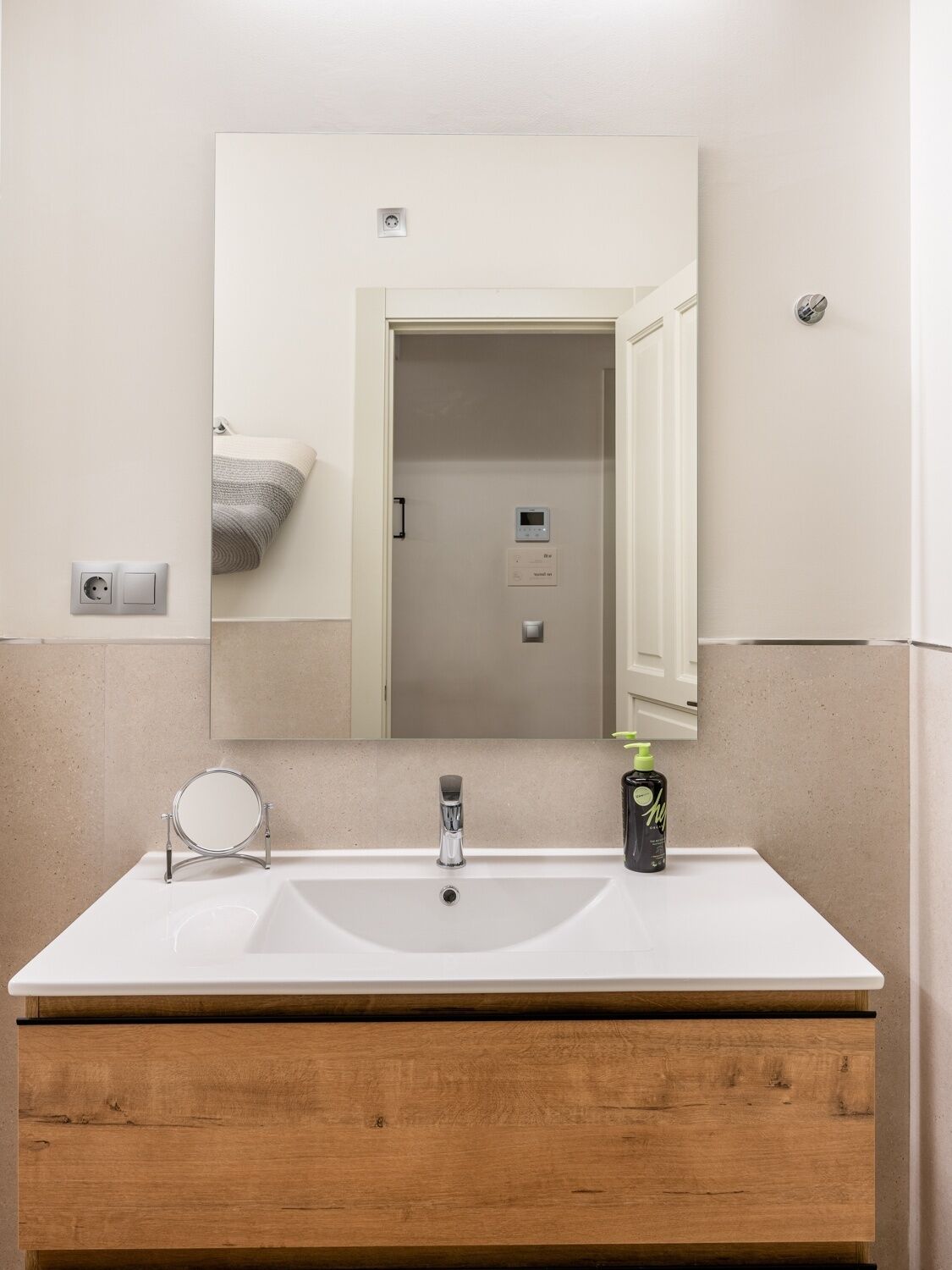 Un baño con lavamanos blanco, espejo y tocador de madera.