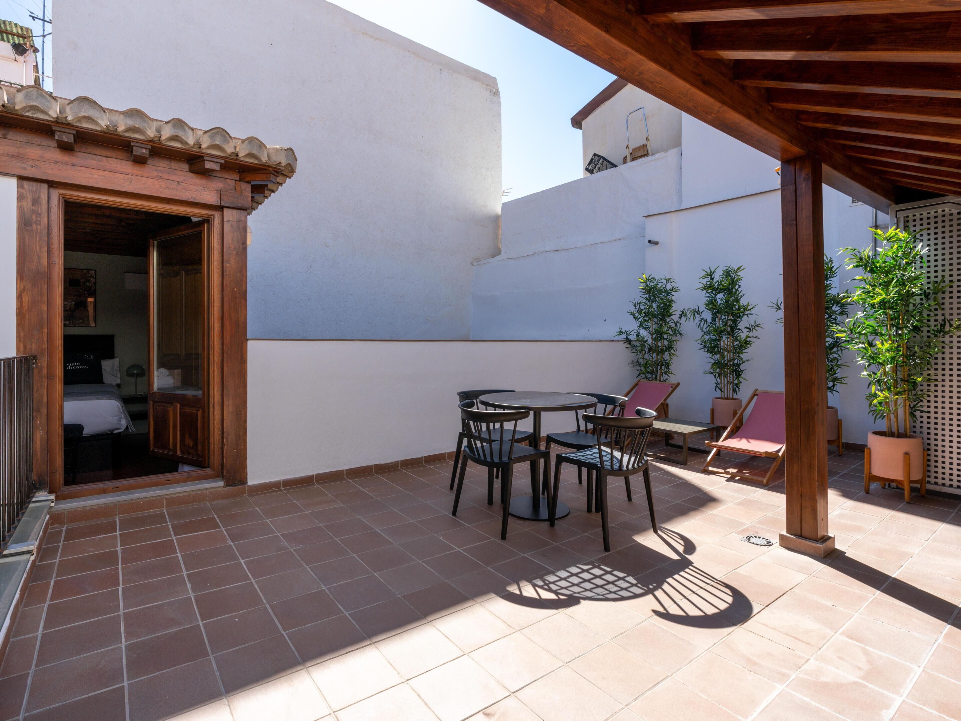 Area patio con pergola in legno, pavimento piastrellato e mobili da esterno.