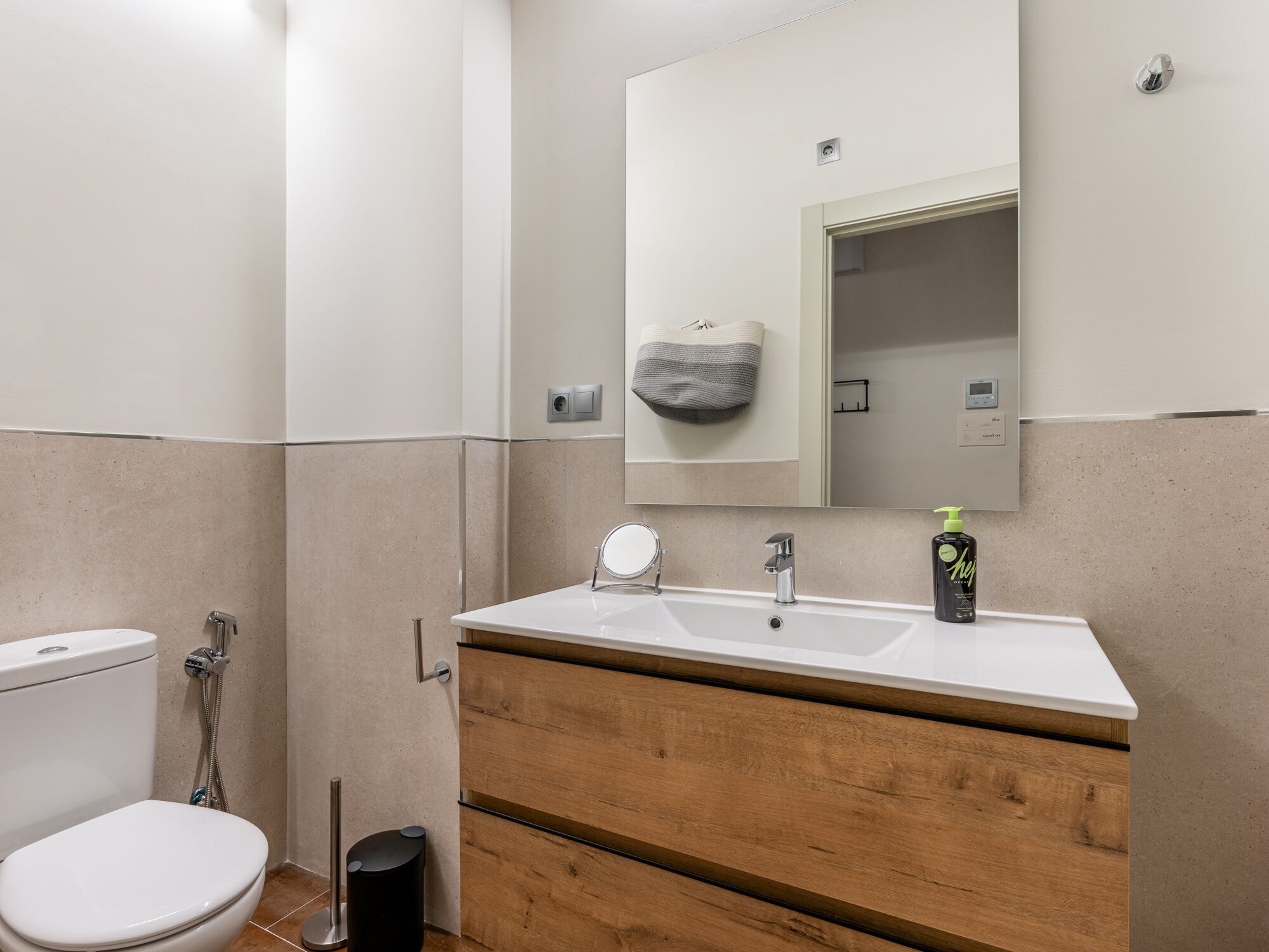 A modern bathroom with a white sink, wooden vanity, and a large mirror.