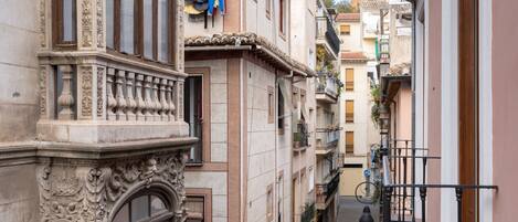 A narrow street with ornate buildings, balconies, and a pedestrian walkway.