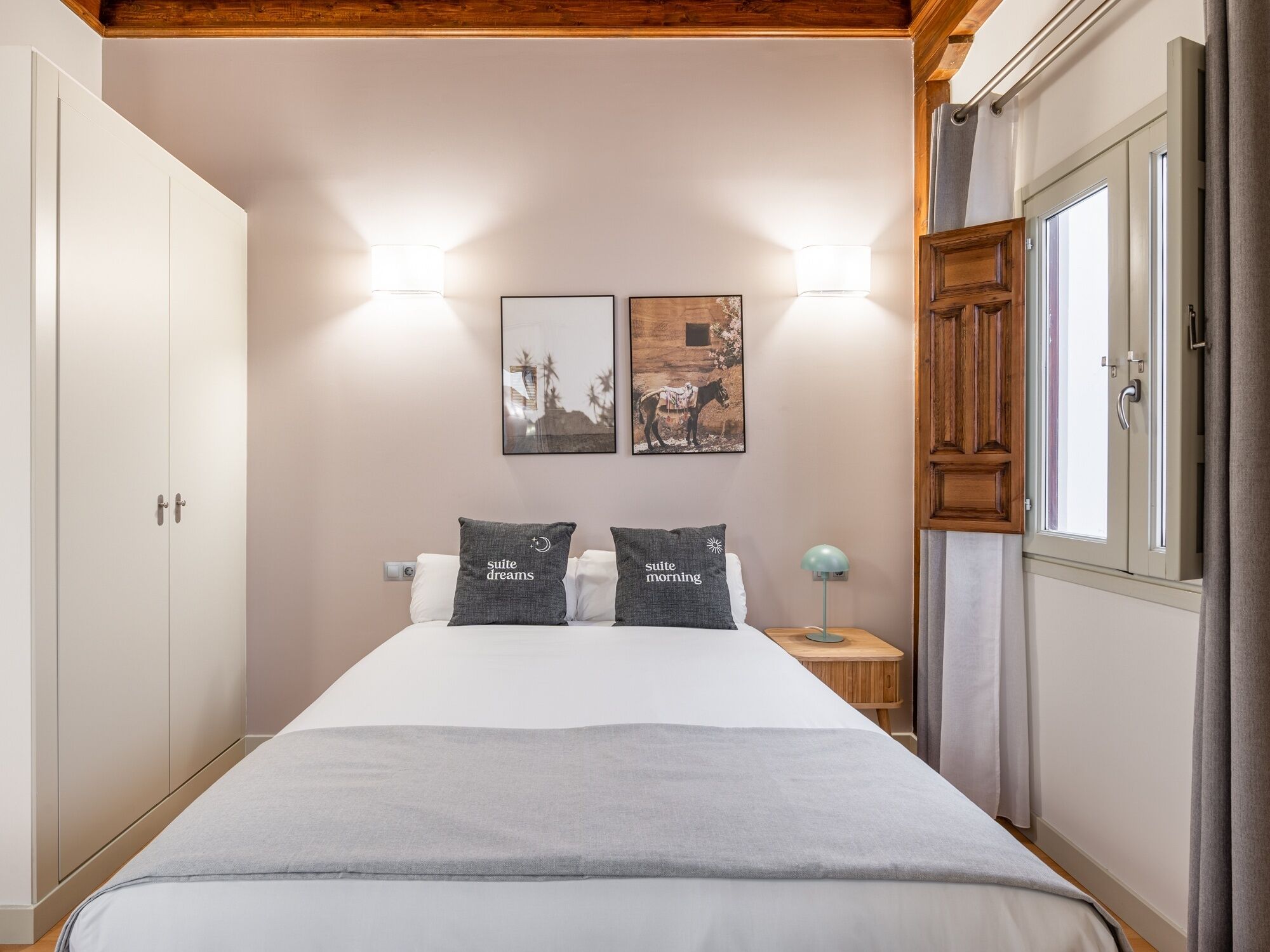 A bedroom with a bed, two bedside lamps, a nightstand, a wardrobe, and two framed pictures on the wall.