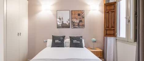 A bedroom with a bed, two bedside lamps, a nightstand, a wardrobe, and two framed pictures on the wall.