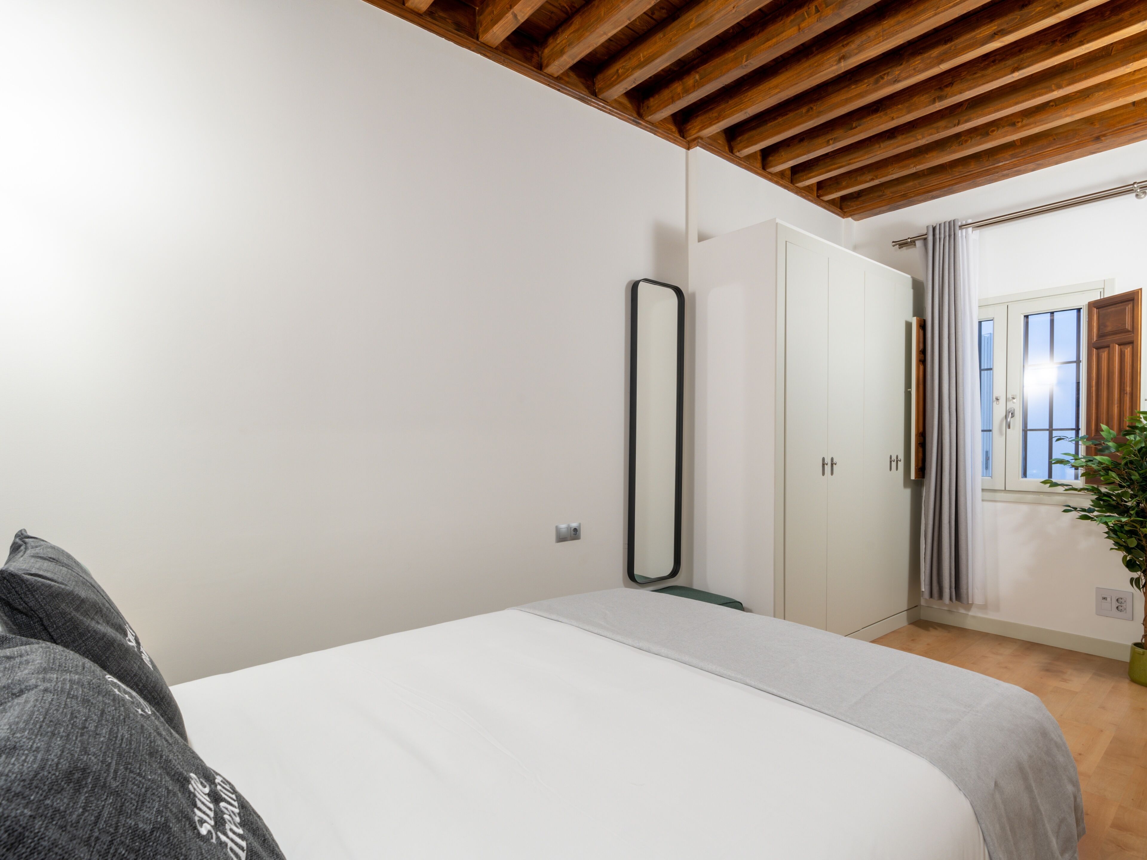 Una camera da letto con soffitto in legno, un letto, un armadio e una finestra con tende.