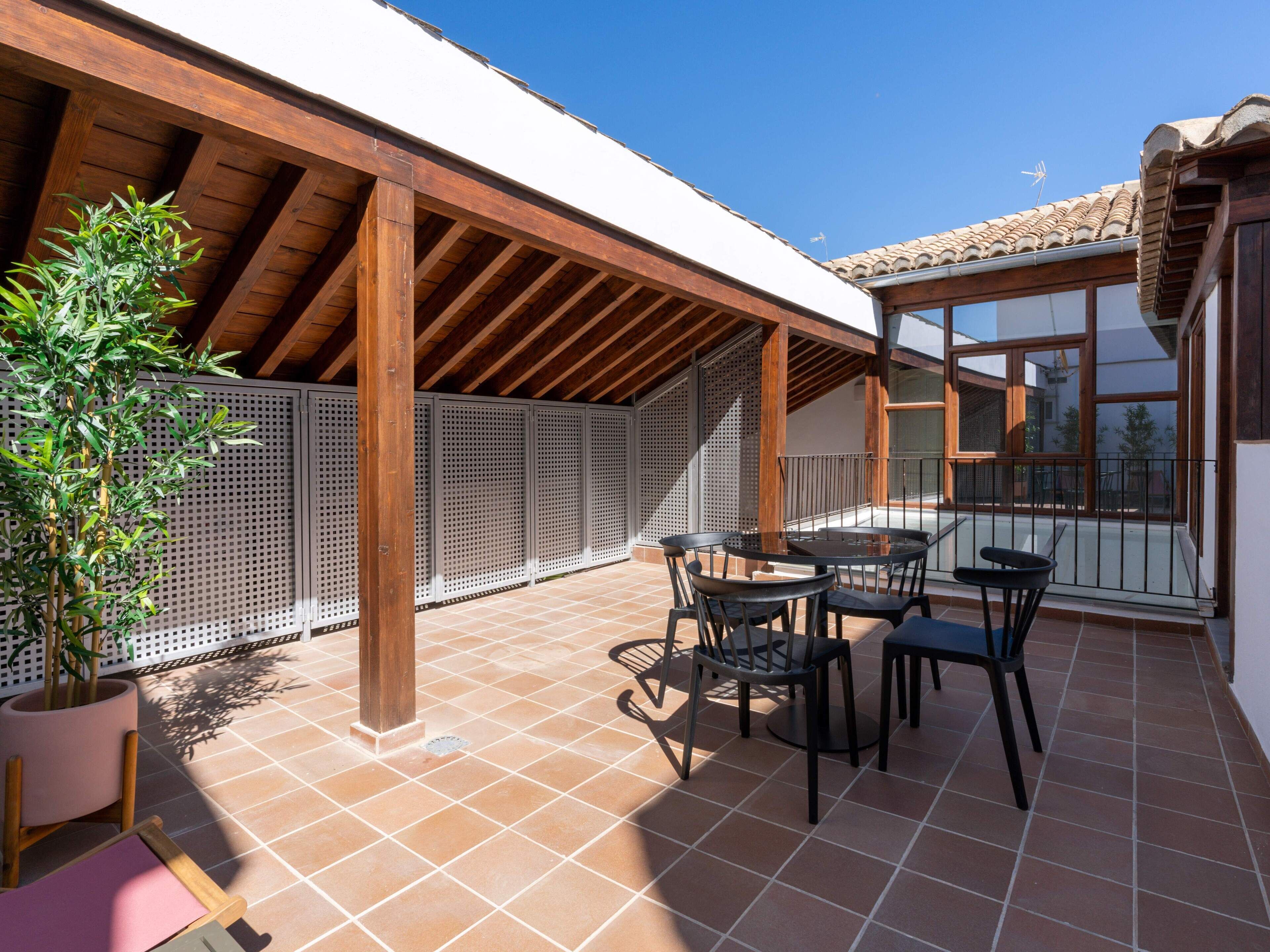 A covered patio with a tiled floor, wooden beams, a pergola, and a table with chairs.