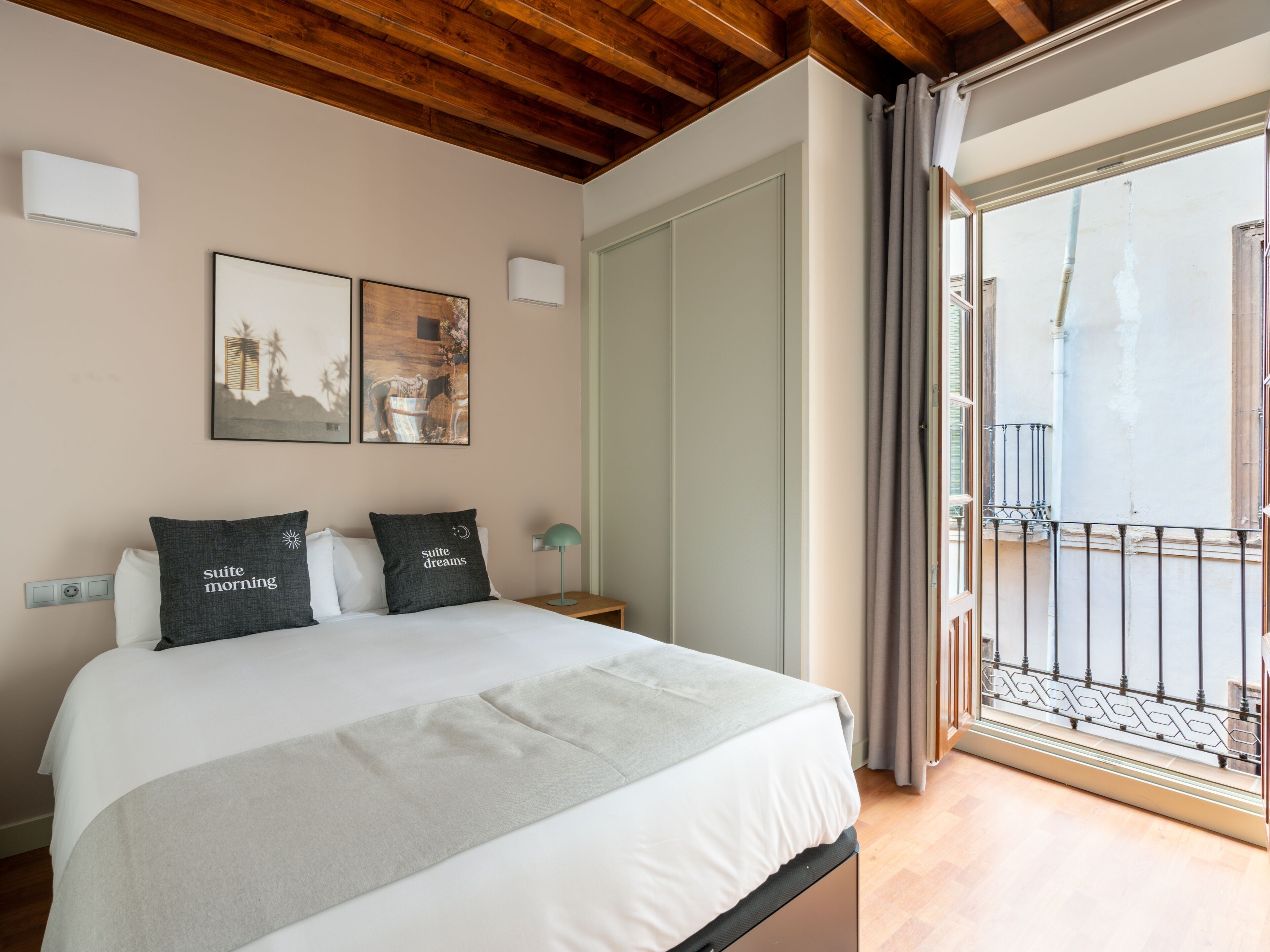 Ein Schlafzimmer mit einem Bett, zwei Kissen, einem Nachttisch mit Lampe, einer Wand-Klimaanlage und einem Fenster mit Ausblick.