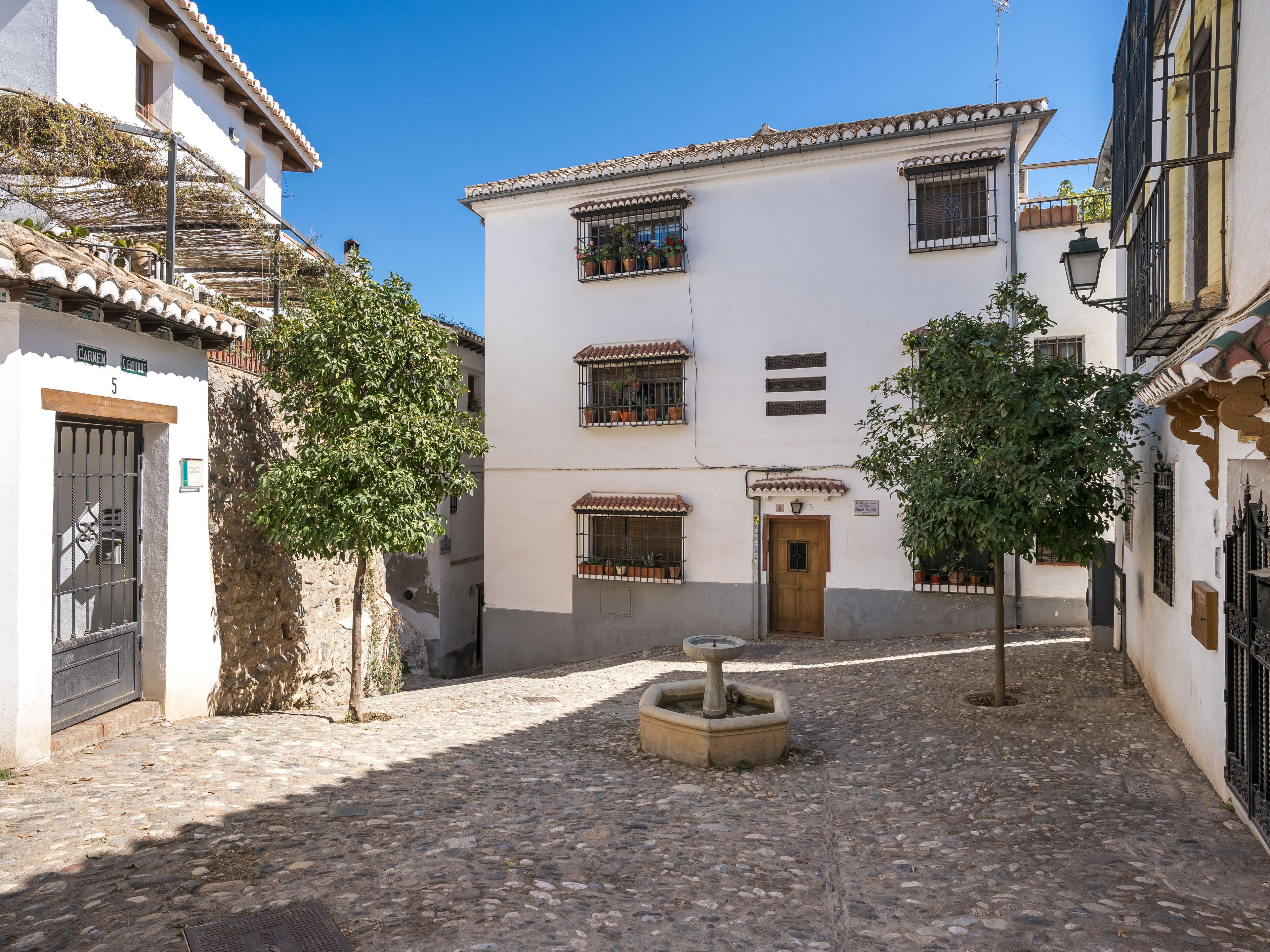 A cobblestone courtyard with a fountain, surrounded by buildings with white walls and terracotta roofs.