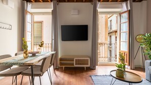 Una sala moderna con techo de madera, un televisor de pantalla plana en la pared, una mesa de comedor con sillas, una mesita auxiliar con una planta y vistas al balcón.
