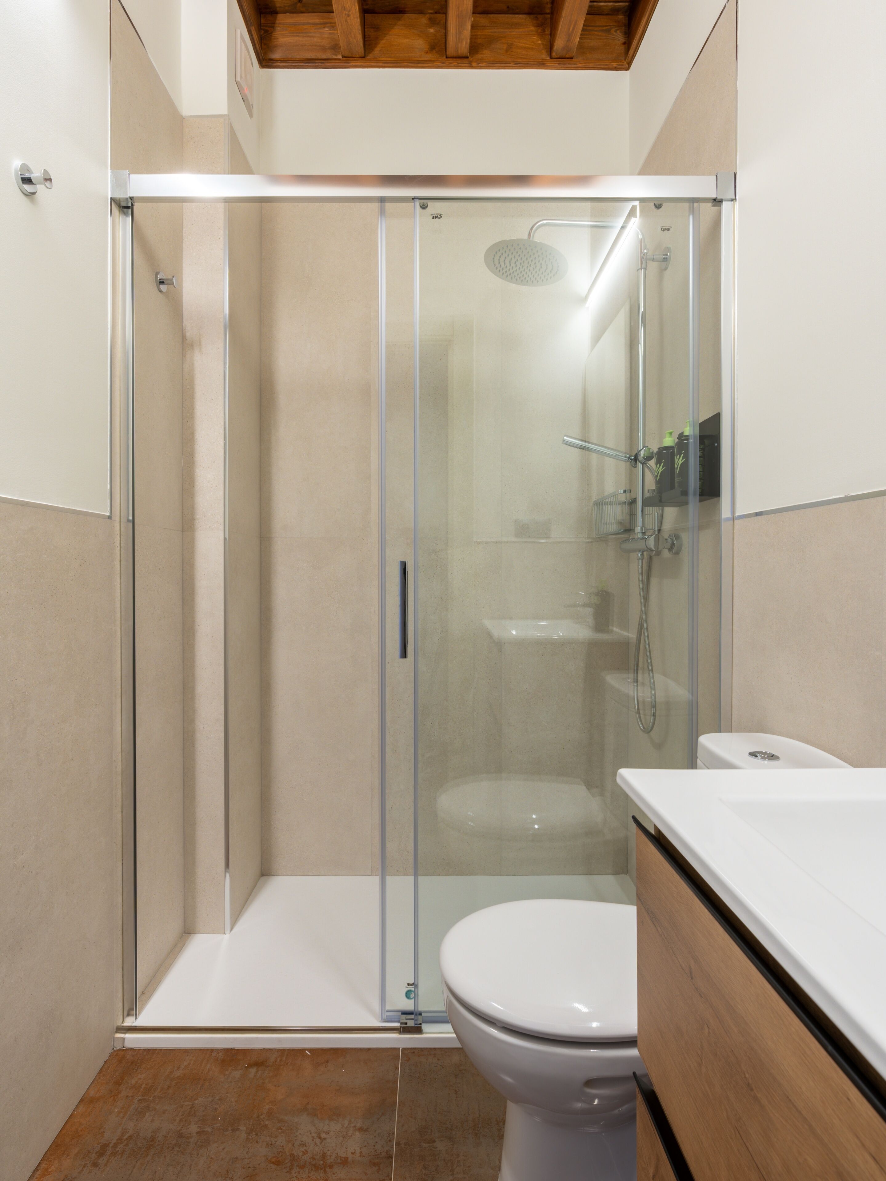 Een moderne badkamer met een glazen douchecabine, een wit toilet en een houten wastafelmeubel.