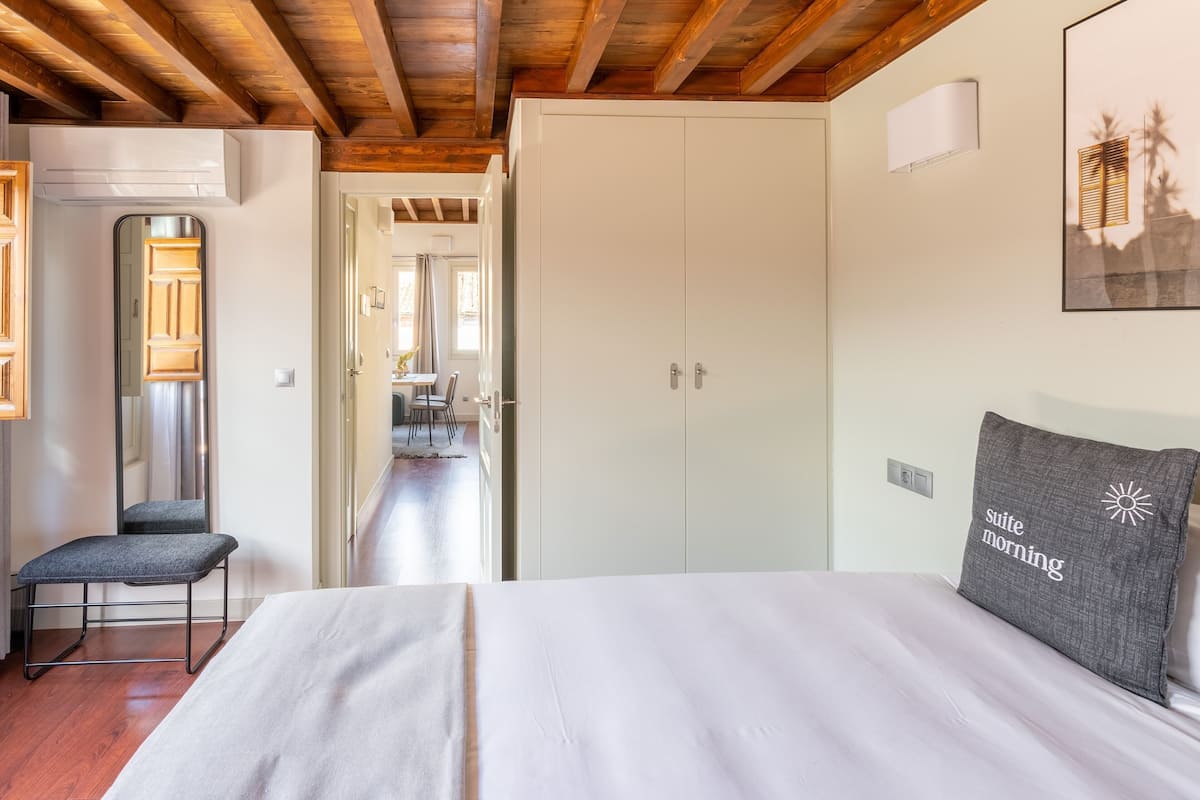 Un dormitorio con cama, una silla, un armario y una puerta que da a otra habitación.