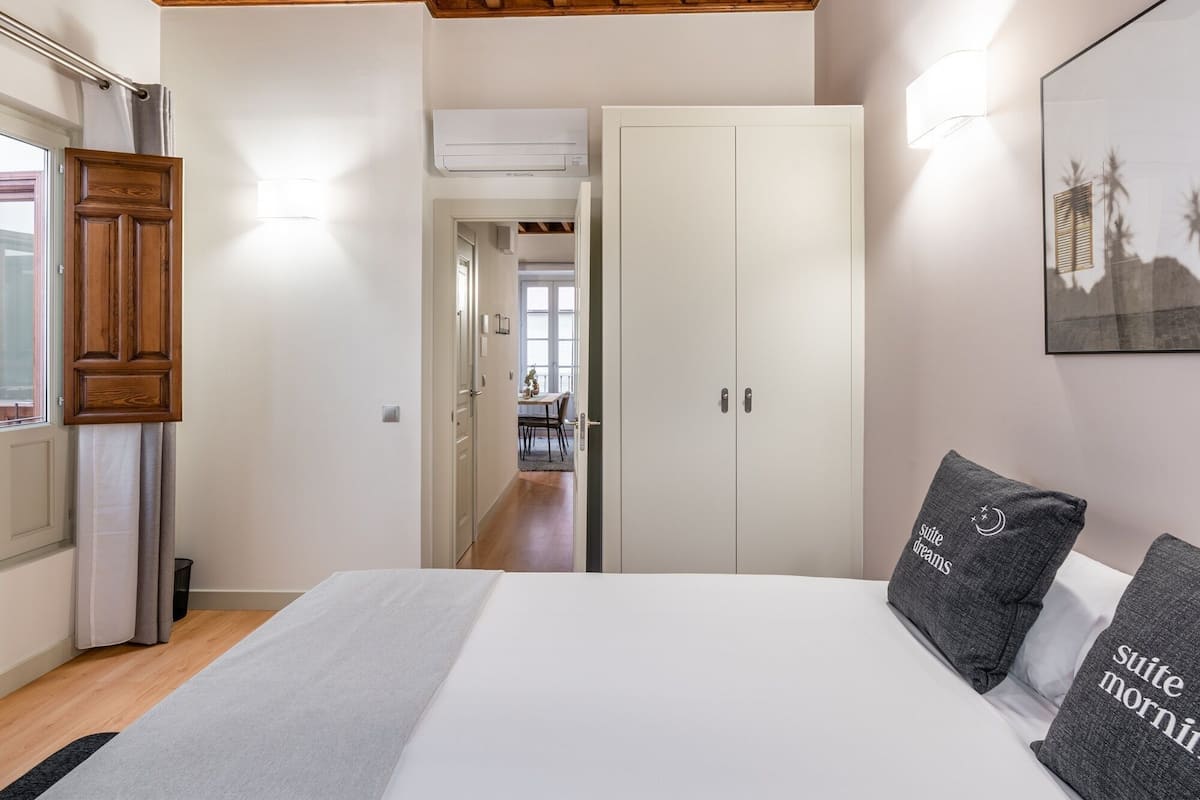 Un dormitorio con techo de madera, una cama con almohadas, un armario y un pasillo que da a una zona de comedor.