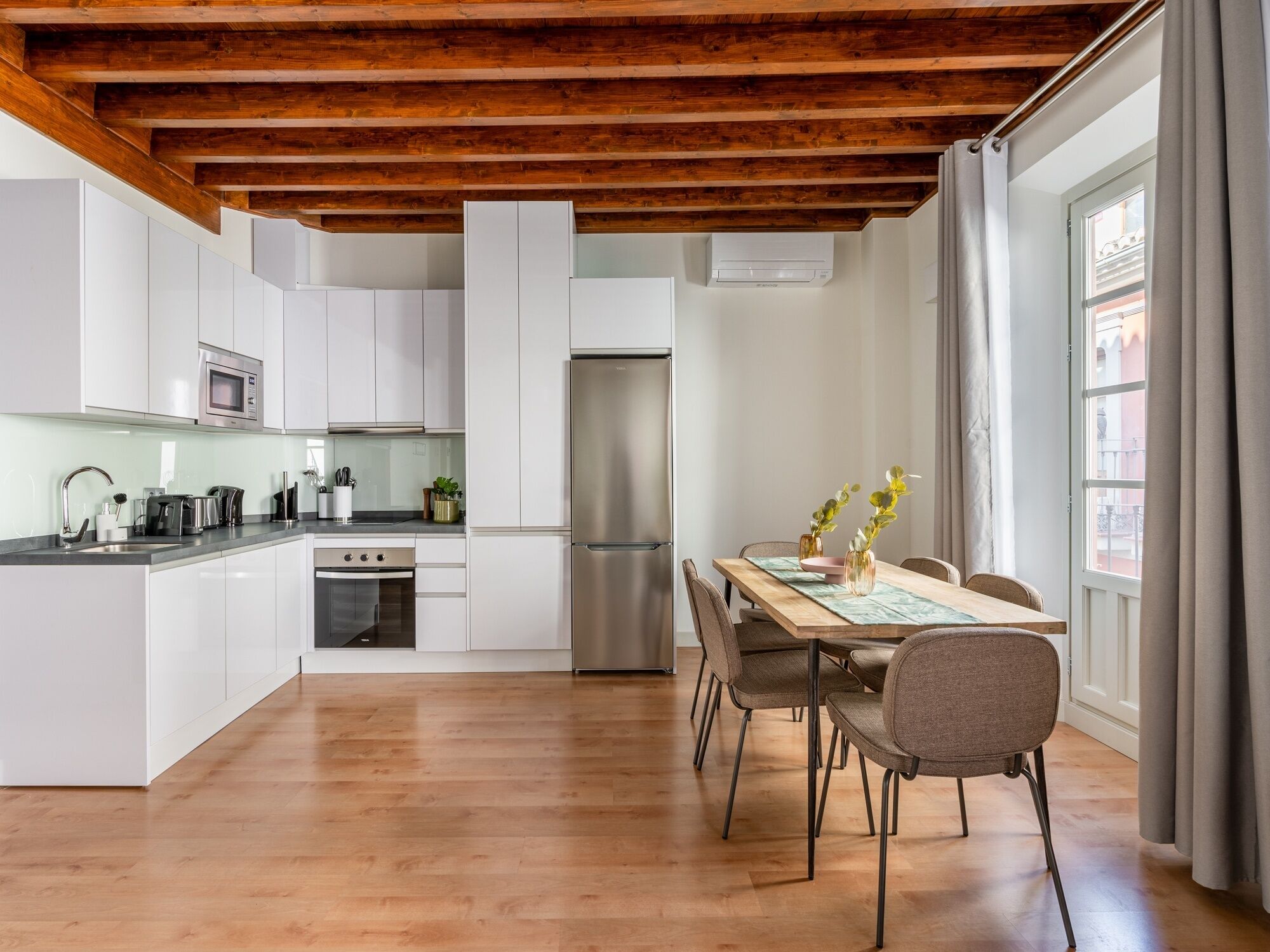 A modern kitchen with white cabinets, stainless steel appliances, and a wooden ceiling.