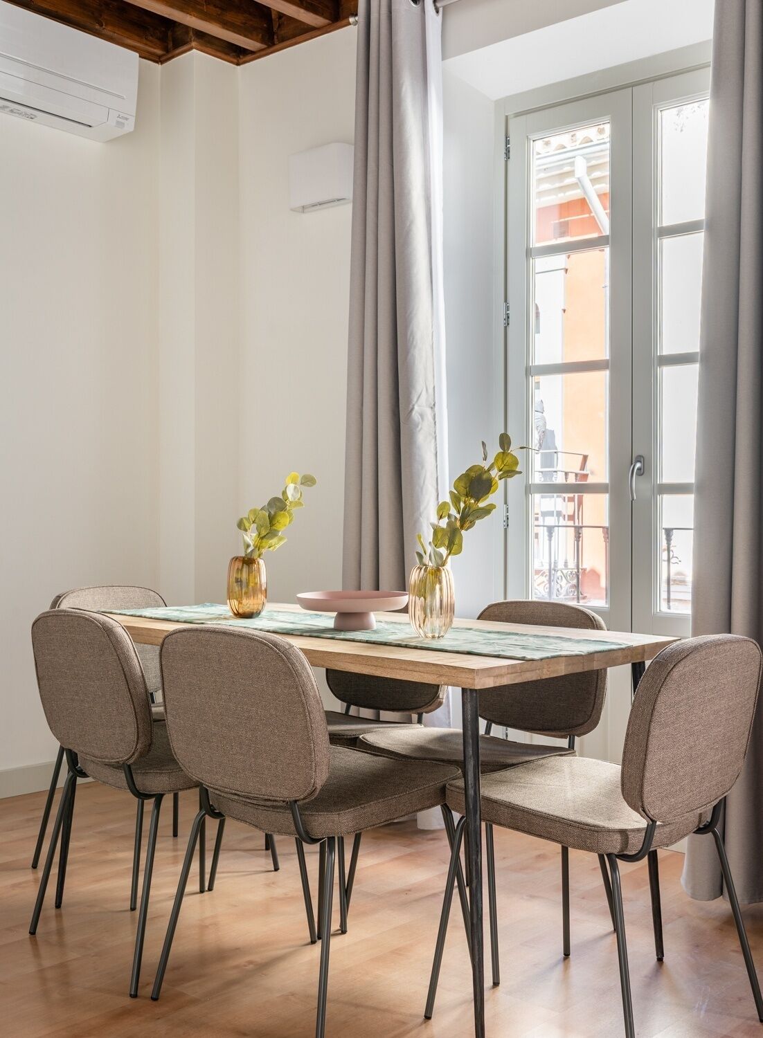 Un comedor con una mesa de madera, cuatro sillas y dos jarrones con plantas.