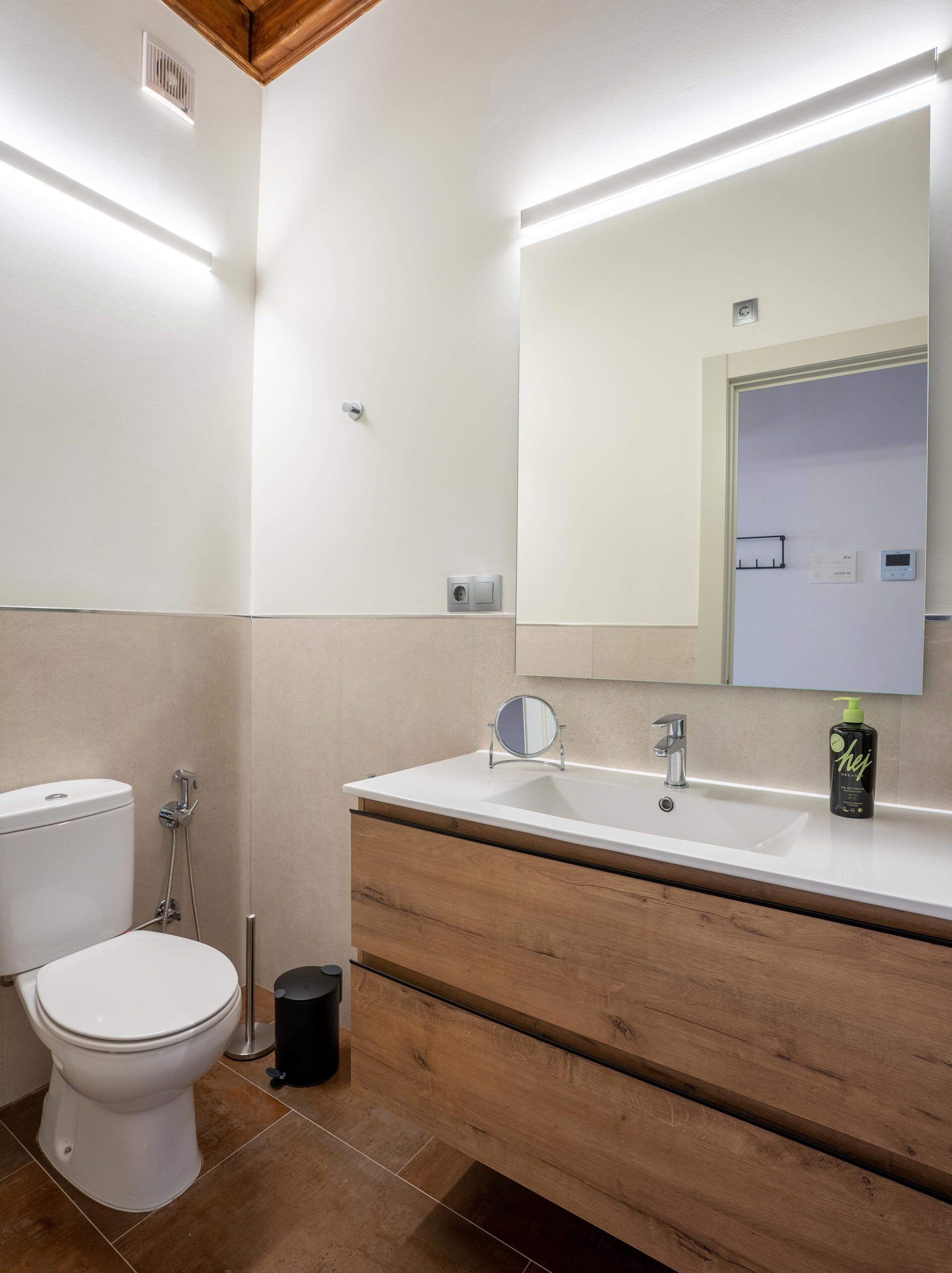 A modern bathroom with a white toilet, a wooden vanity with a mirror, and a white sink.