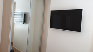 A room with a flat-screen TV mounted on the wall, a window with blinds, and a door with a mirror. - London Luxury 3 Bedroom Apartment 1 min from Redbridge Tube Station (London)
