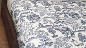 A bed with a blue and white patterned bedspread and pillows, a wooden headboard, and a bedside table with a remote control. - London Luxury 3 Bedroom Apartment 1 min from Redbridge Tube Station (London)