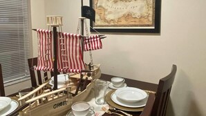 Un tavolo da pranzo con una nave pirata in miniatura, una mappa incorniciata e stoviglie.